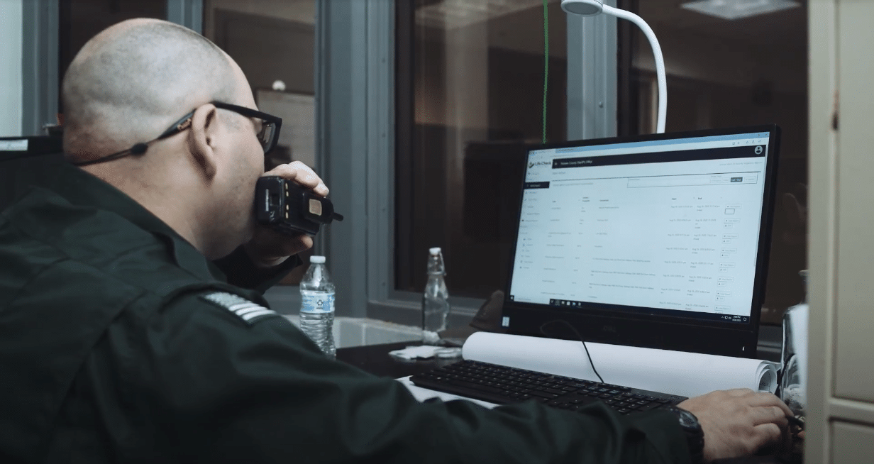 Corrections officer speaking into walkie talkie while monitoring jail security from a computer using Life Check Systems