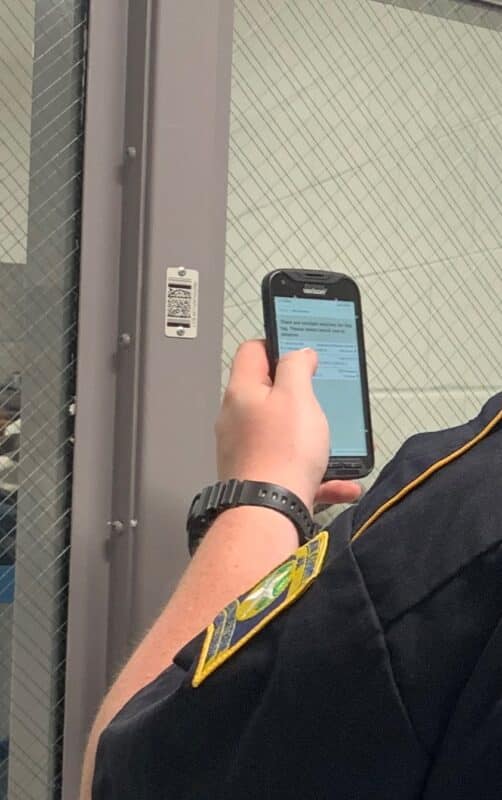 Corrections officer holding up a mobile phone using Life Check Systems next to an NFC tag on door frame