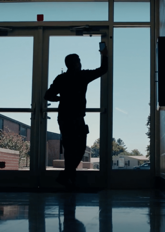 School resource officer holding phone using Life Check Systems up to an NFC tag on a school door