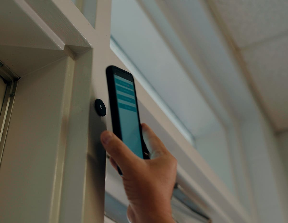 Hand holding phone using Life Check Systems next to NFC tag on school door frame