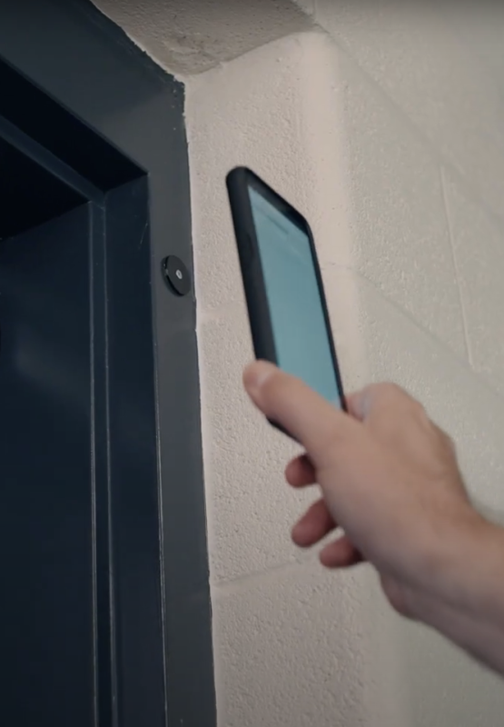 Hand hovering mobile phone next to NFC tag on school door frame